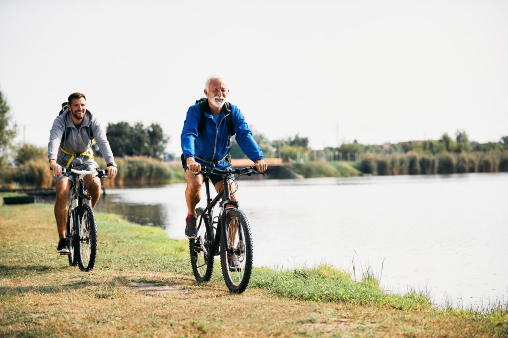 Happy senior athlete and his son riding bicycles by the lake in nature.