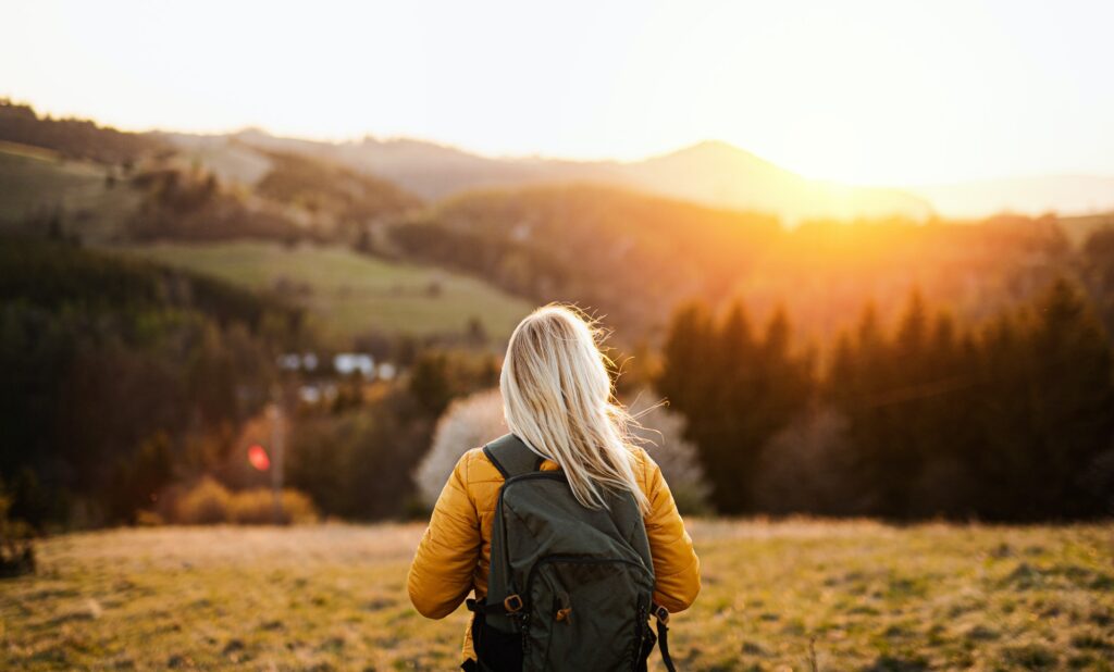 Rear view of senior woman walking outdoors in nature at sunset, hiking