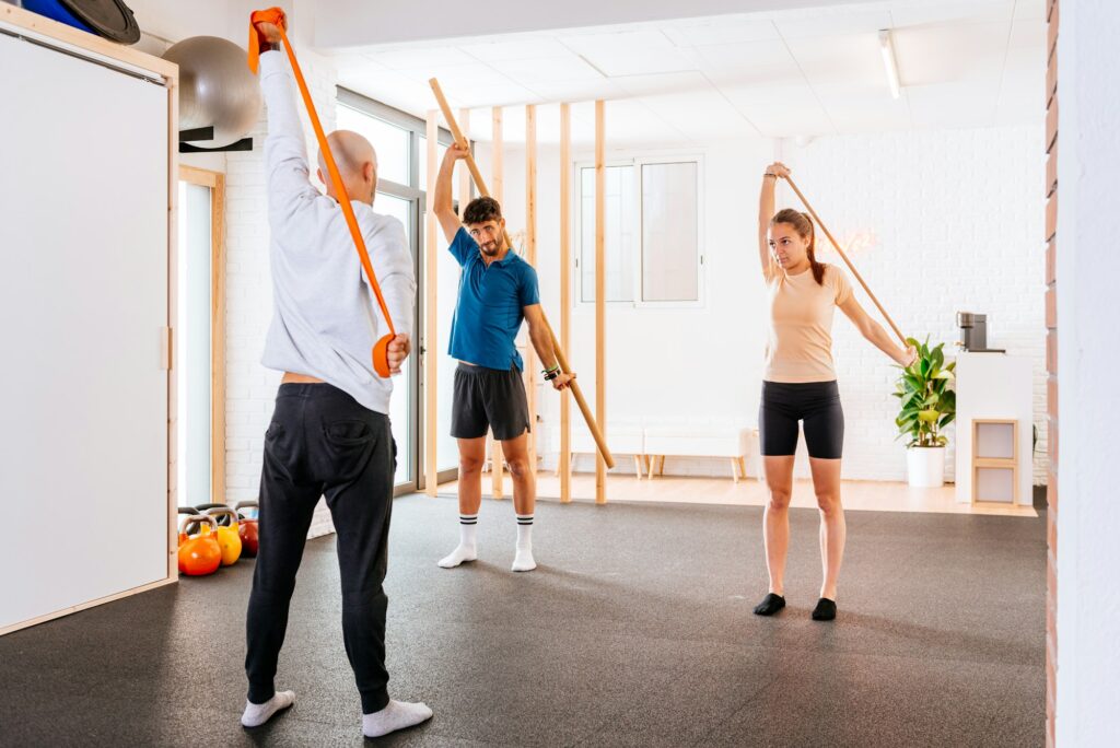 Young man and woman doing mobility routine class with wooden stick in fitness studio